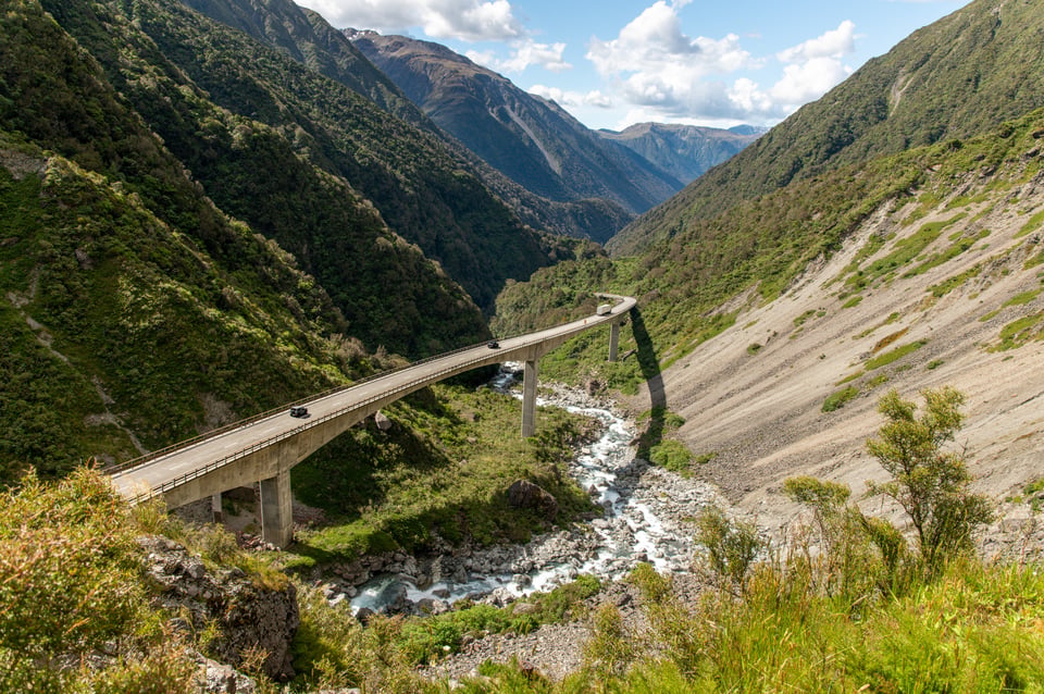 Samochody na łukowatym wiadukcie Otira nad kamienistą rzeką w górach Arthur's Pass w Nowej Zelandii.
